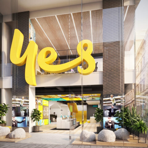 Flagship retail facade, double-height glass storefront, sculptural yellow branding, timber batten ceiling, integrated planter boxes, stone organic seating, digital display entry.